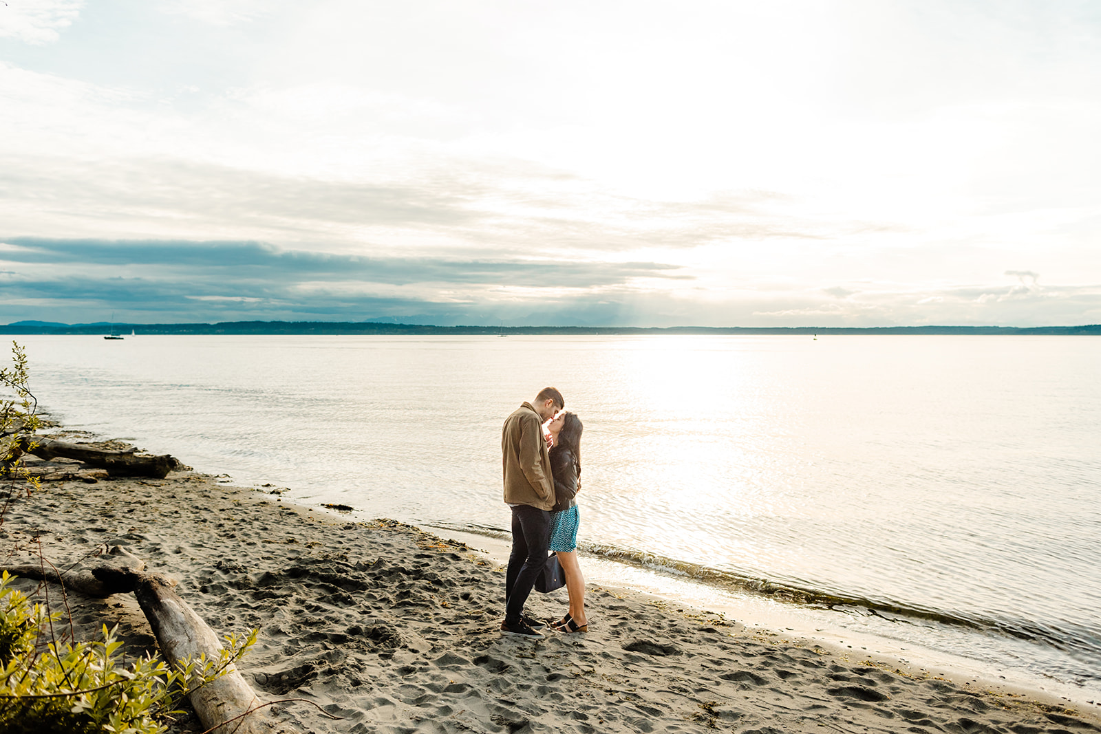 man and woman kiss on beach with ocean behind them
