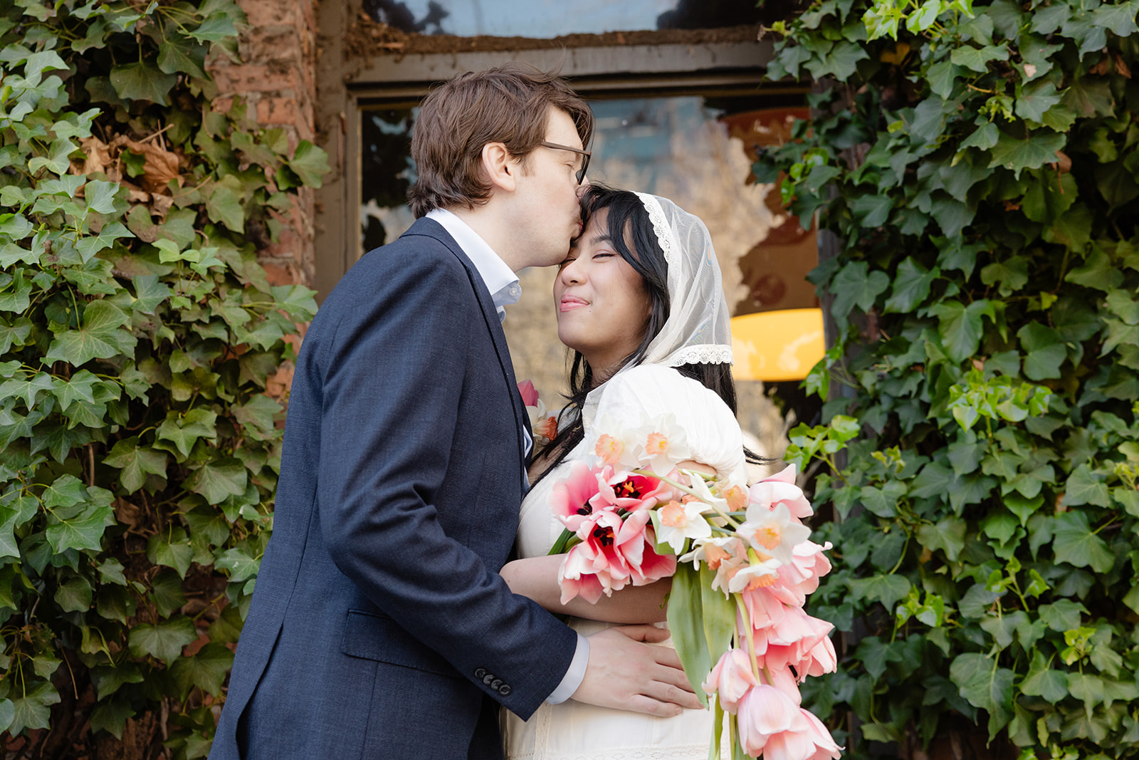 couple kisses in front of ivy wall
