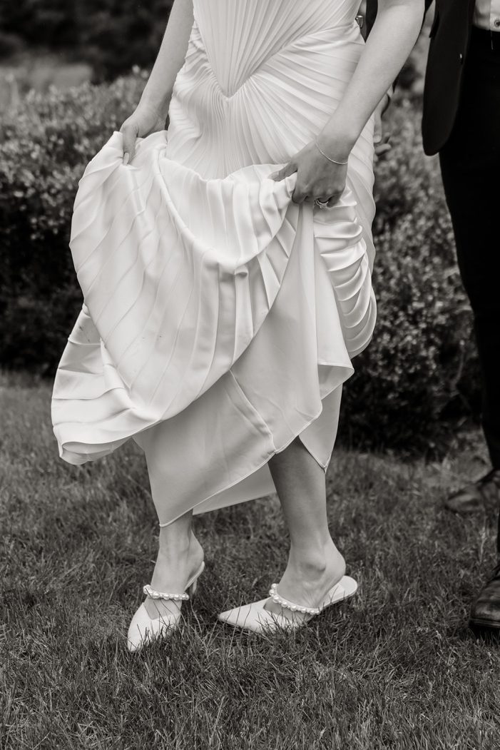 bride lifts her dress as she walks through garden