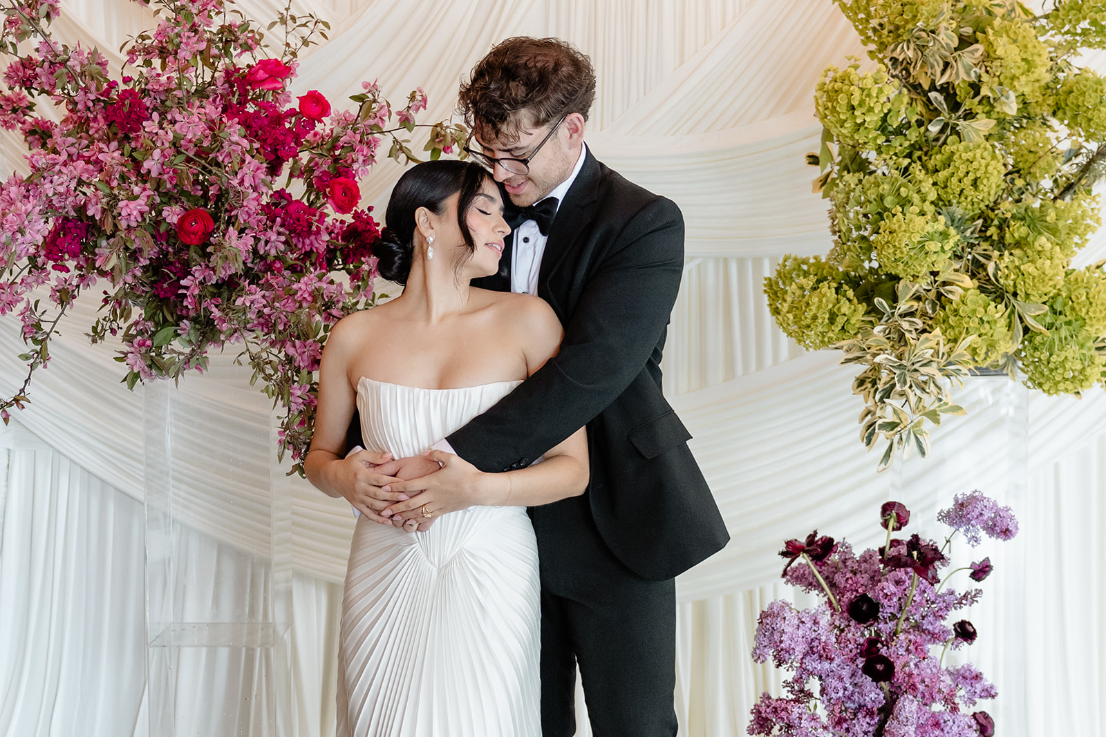 bride and groom are entangled in front of white backdrop