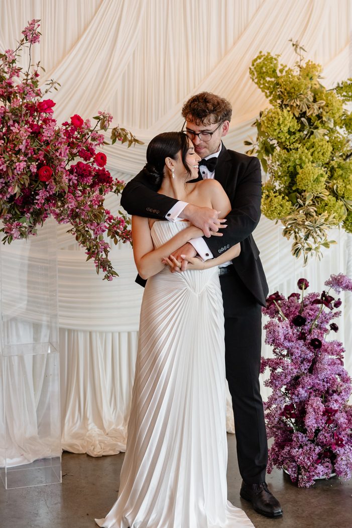 bride and groom are entangled in front of white backdrop