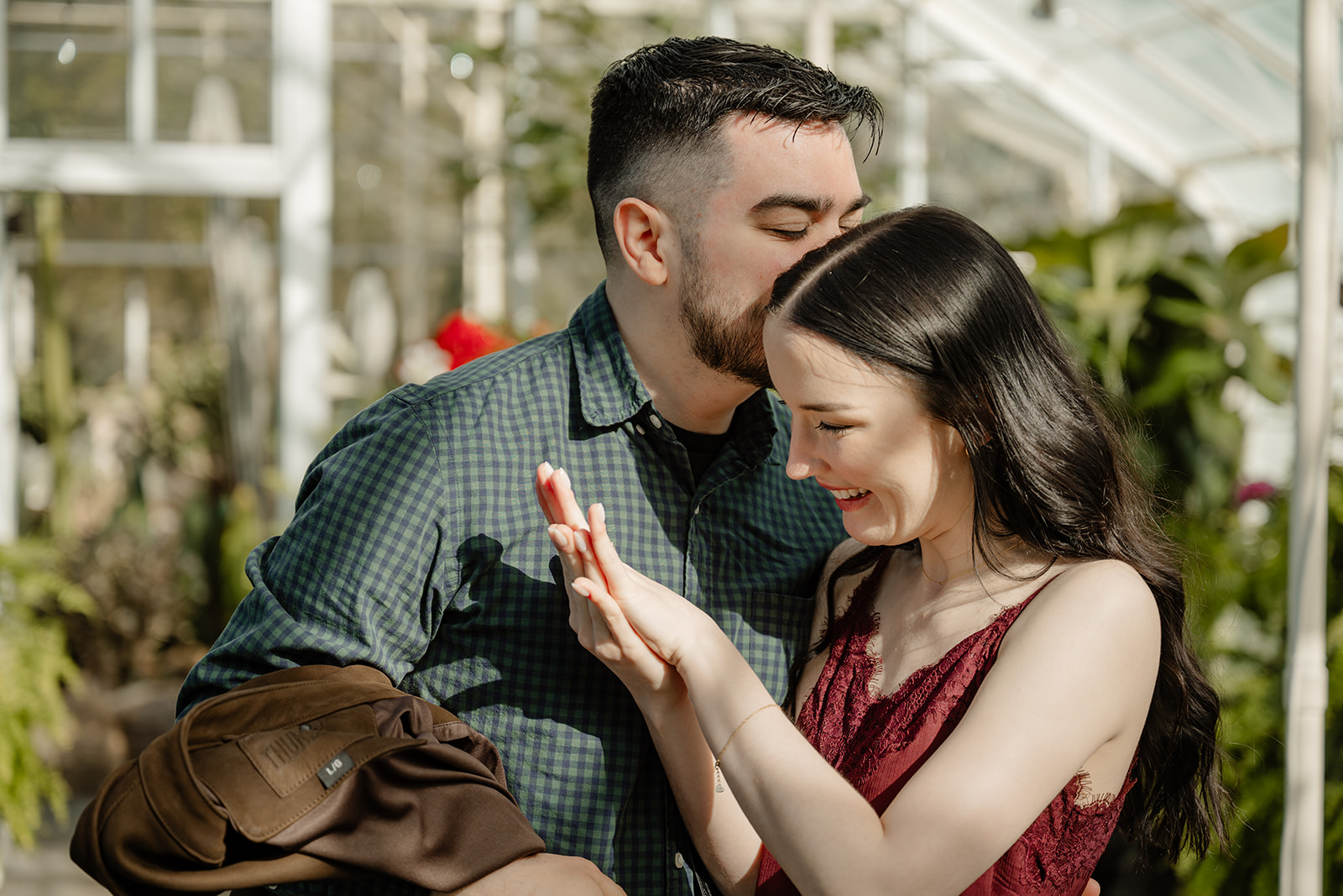 woman looks at engagement ring while man kisses her